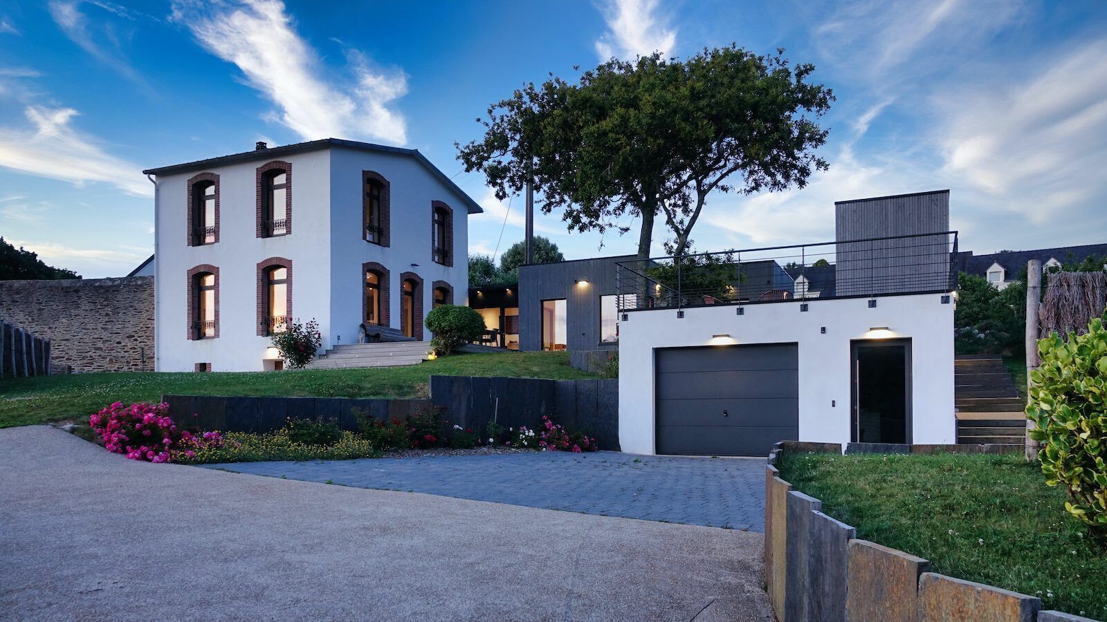 A modern two-story house with a garage, a well-maintained lawn, and a large tree.