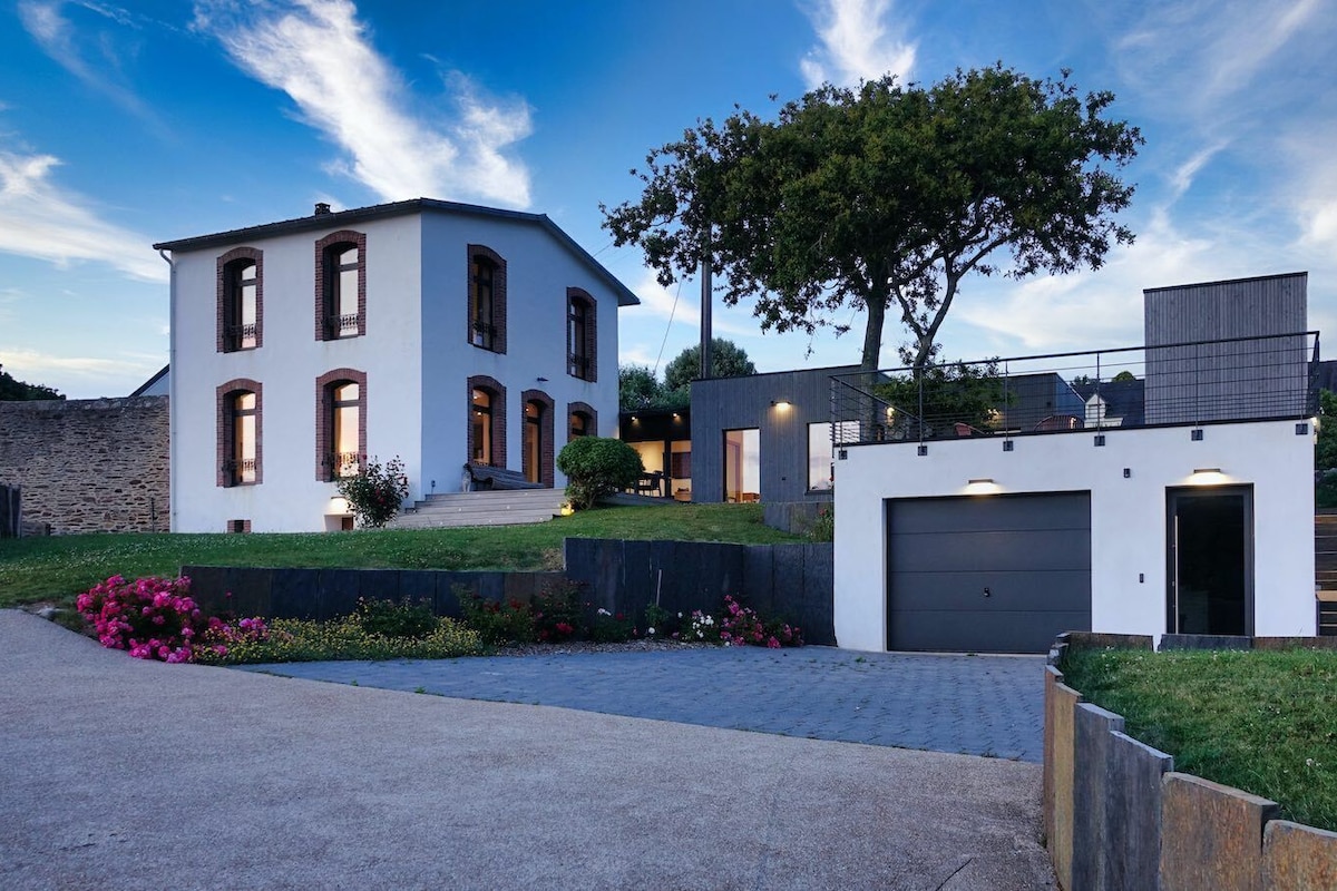 Una casa moderna de dos pisos con garaje, césped cuidado y un árbol grande.