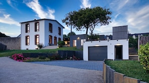 Une maison moderne à deux étages, dotée d’un garage, d’une pelouse bien entretenue et d’un grand arbre.