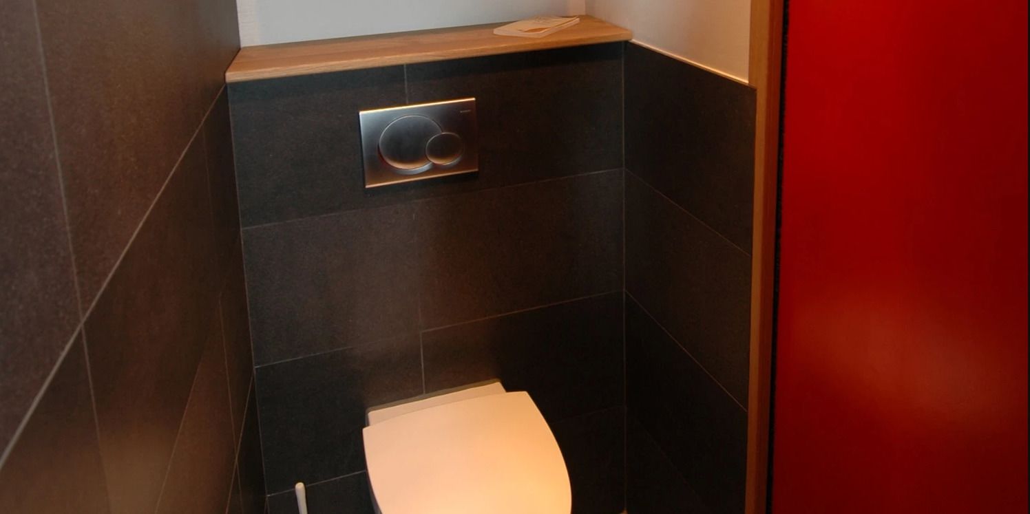 A modern bathroom with a toilet, a flush handle, and a wooden counter.