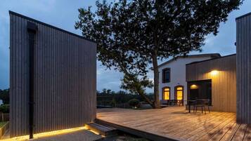 Un bâtiment moderne doté d’une terrasse en bois, d’un grand arbre et d’une entrée bien éclairée.