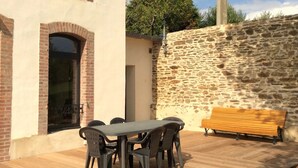 Een terras buiten met een tafel en stoelen, een houten bank en een stenen muur.