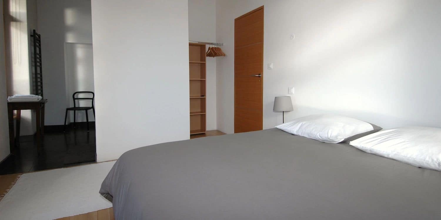 A bedroom with a bed, a chair, a wardrobe, and a bedside table.