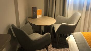 Una habitación de hotel con cama, dos sillones, una mesita y una mesita de noche.
