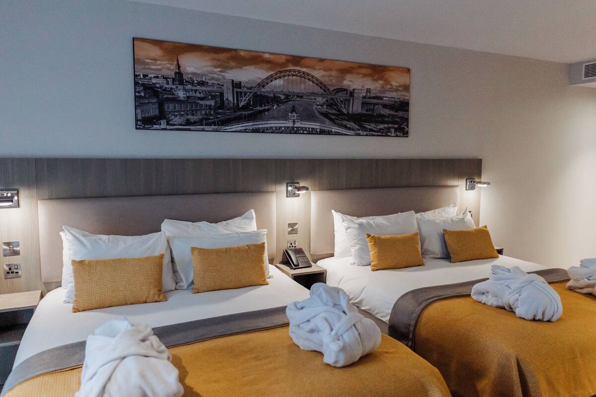 A hotel room with two beds, a painting of a bridge, and a telephone on the nightstand.