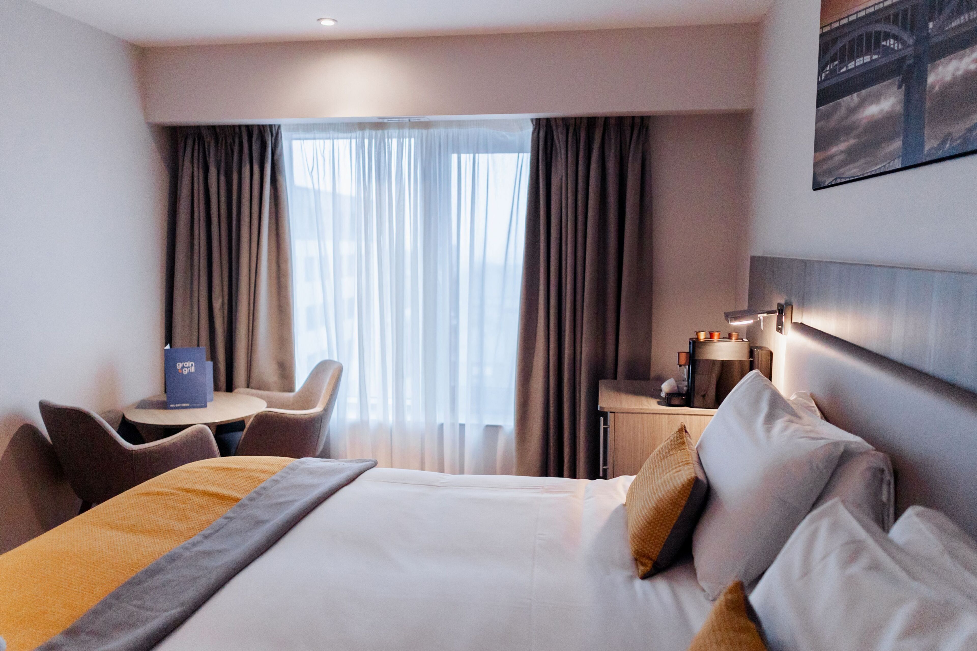 A hotel room with a bed, a desk, a chair, and a view of a bridge through the window.