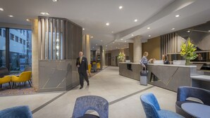 A modern hotel lobby with a reception desk, seating area, and a staircase. - Maldron Hotel Newcastle (Newcastle-upon-Tyne)