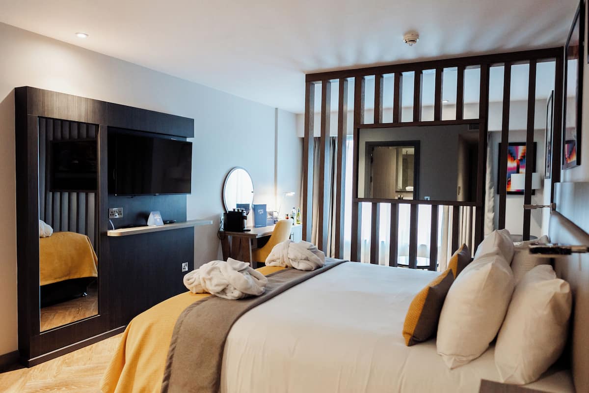 A hotel room with a bed, a desk, a television, and a mirror.