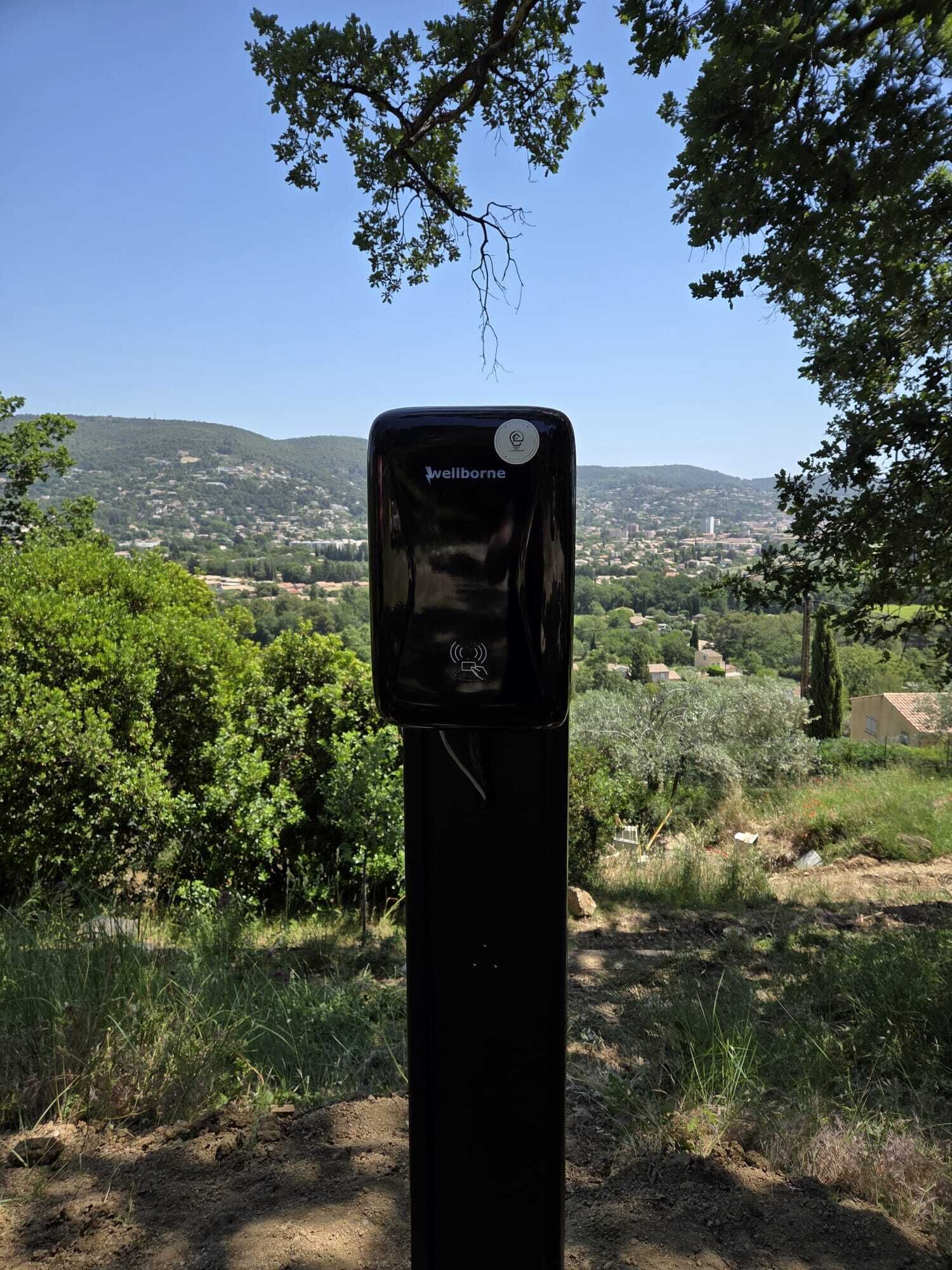 A black Wellborne charging station in a natural setting with a view of a hilly landscape.