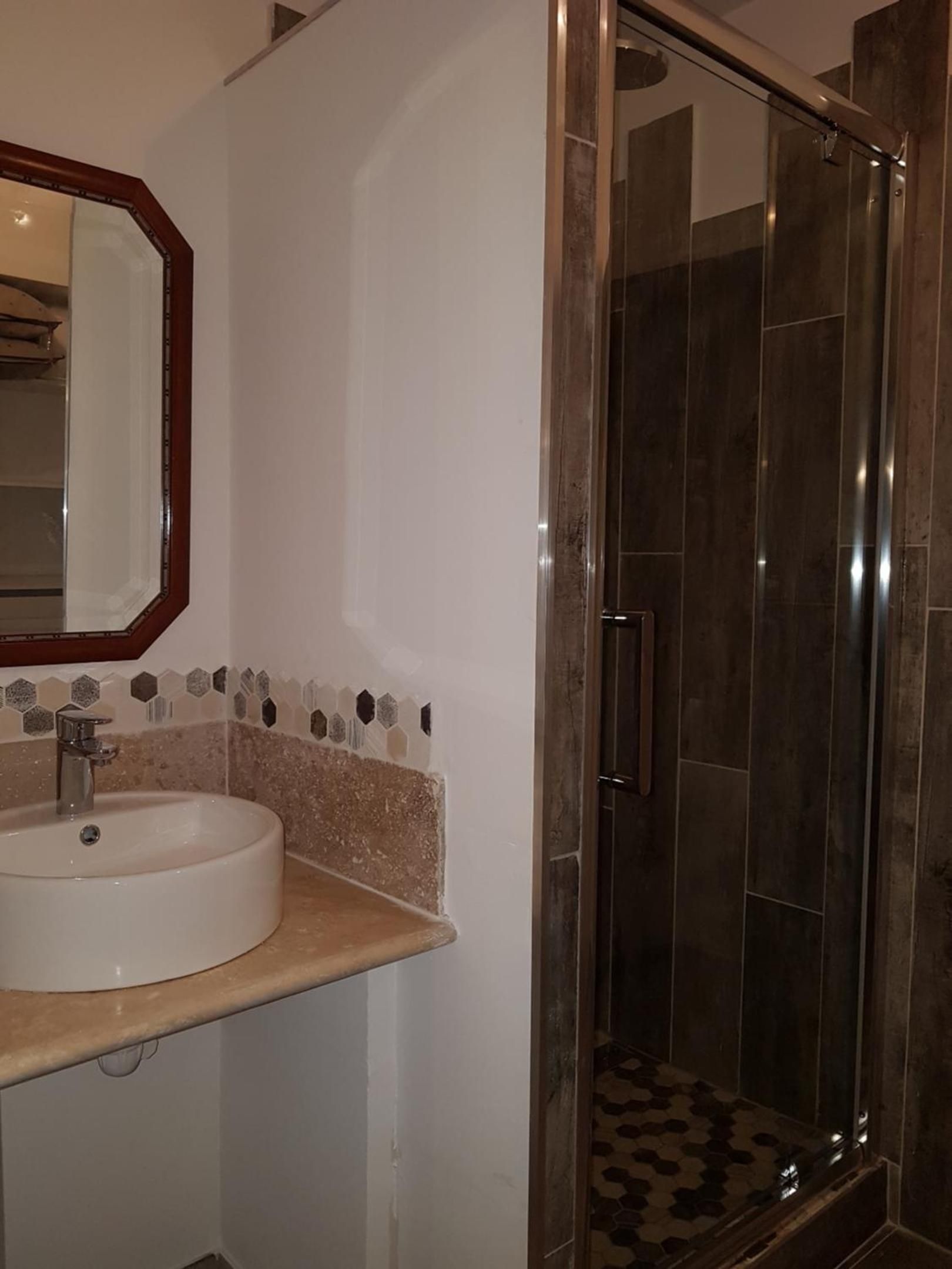 Un baño con lavamanos blanco, un espejo y una ducha con puerta de vidrio.