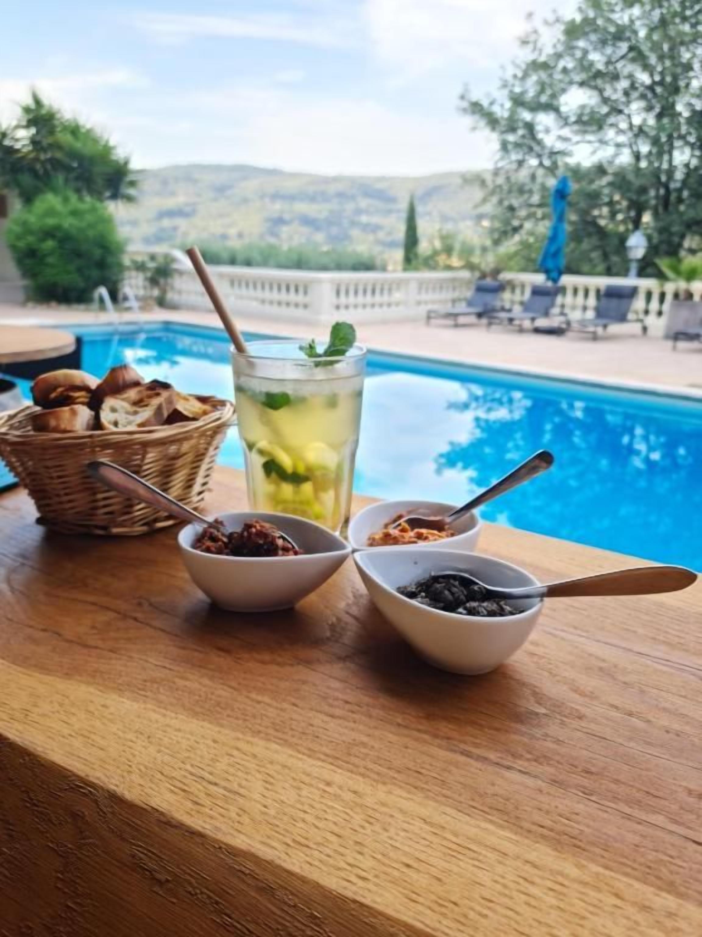 A poolside table with a drink, bowls of condiments, and a basket of bread.