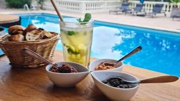 Una mesa junto a la piscina con una bebida, recipientes de salsas y una cesta de pan.