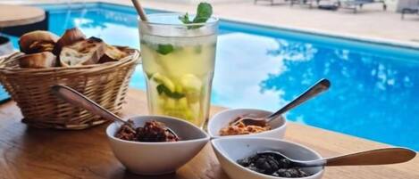 A poolside table with a drink, bowls of condiments, and a basket of bread.