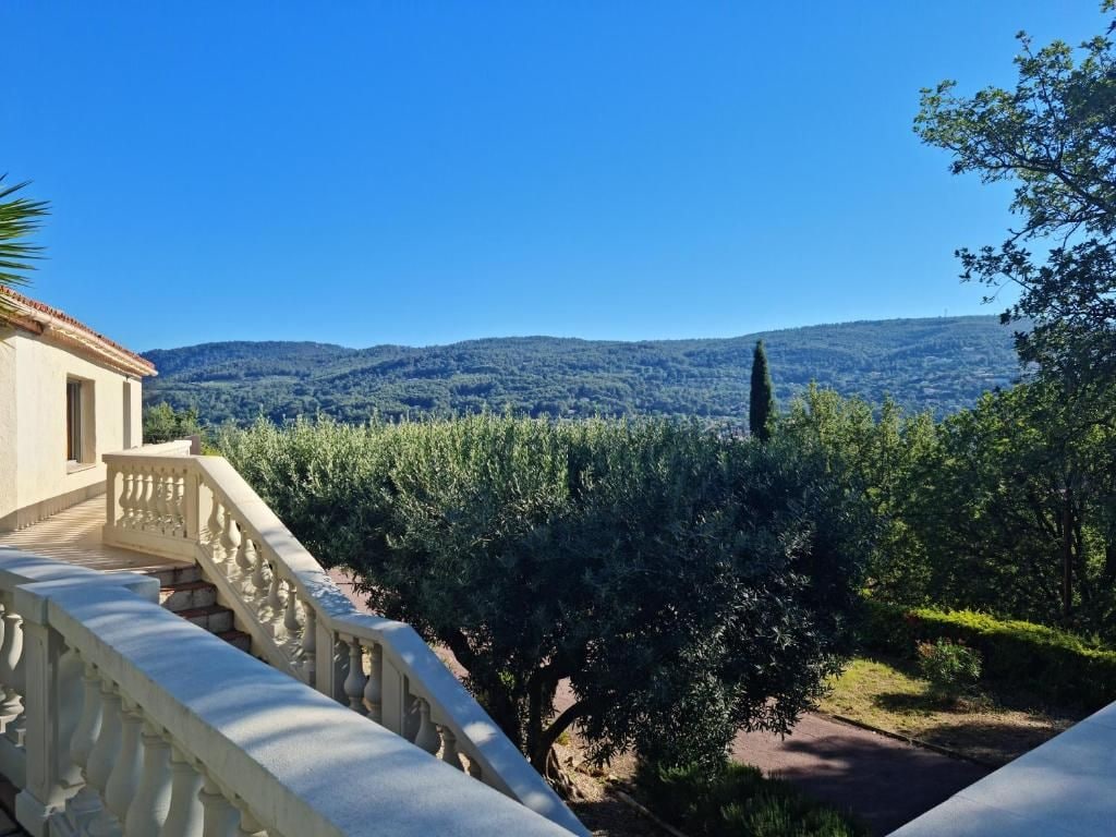 A building with a balcony overlooking a vineyard and distant hills.