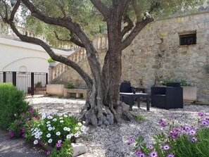 A stone building with a large tree in the center, outdoor seating, and a gravel ground. - Villa Manoé (Draguignan)