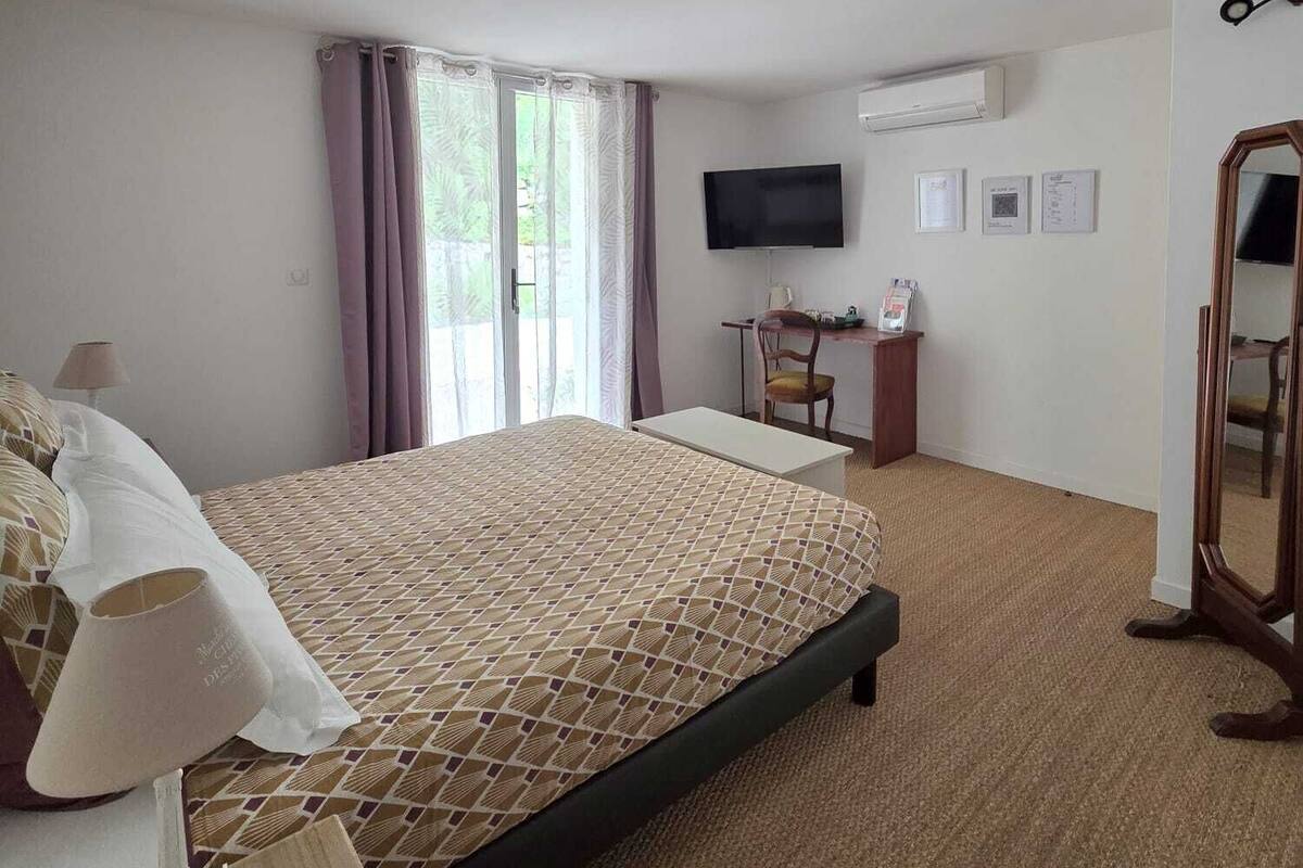 A hotel room with a bed, a desk, a chair, a TV, and a mirror.