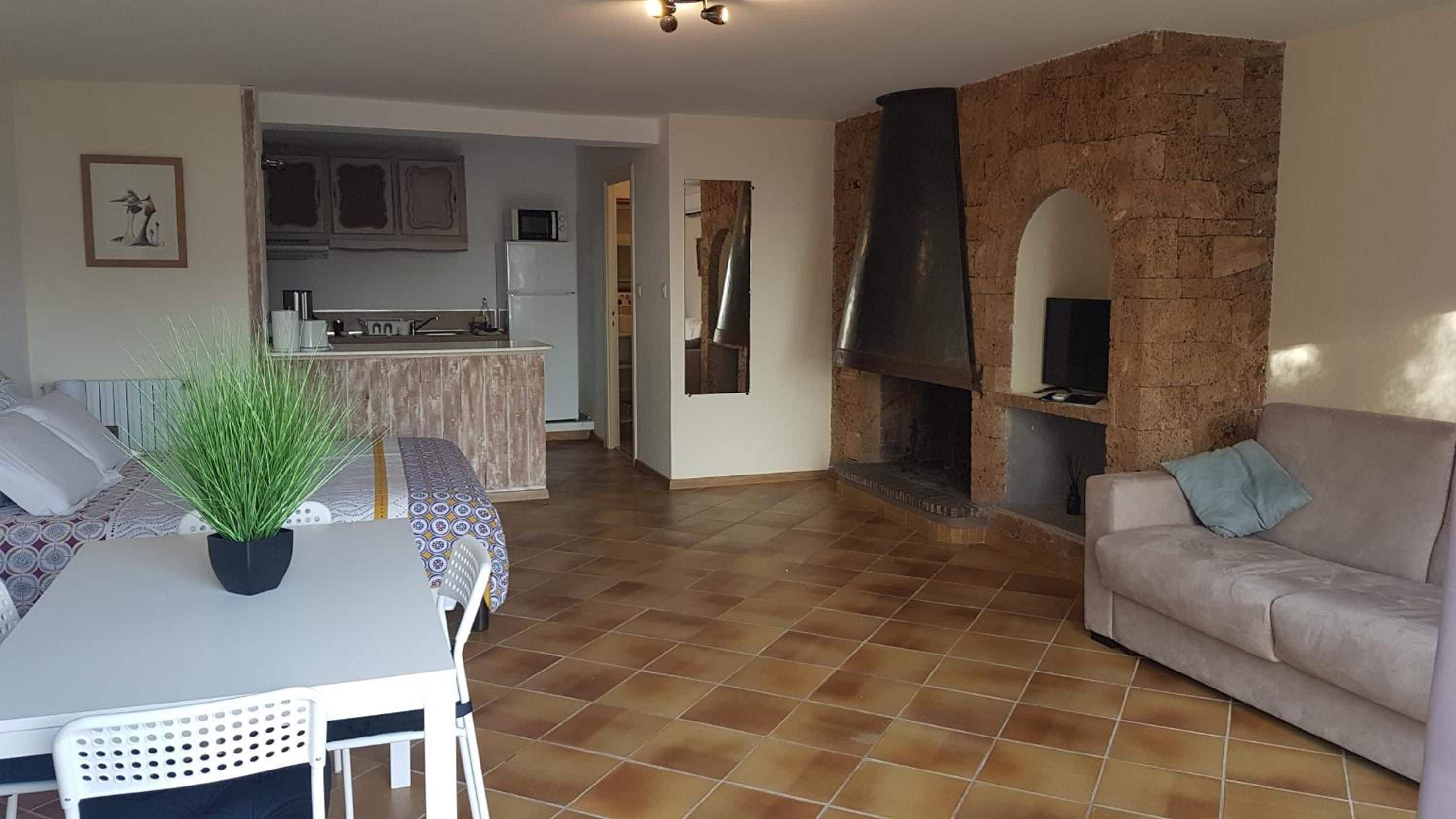 Un salon avec un canapé, une table à manger et des chaises, un coin cuisine et une cheminée en pierre.
