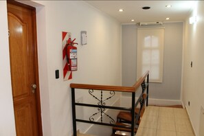 Un escalier avec une main courante en bois et des balustrades en métal, un extincteur fixé au mur et une porte avec un cadre en bois.
