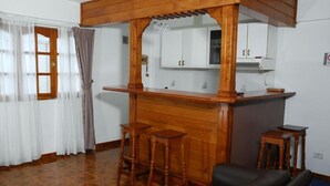 A kitchen with wooden bar stools, a black leather sofa, and a window with curtains. - Ushuaia Apart Hotel Cabo San Diego (Ushuaia)