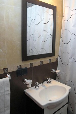 Une salle de bain avec un lavabo blanc, deux robinets, un miroir avec un cadre noir et un rideau de douche à motifs ondulés.