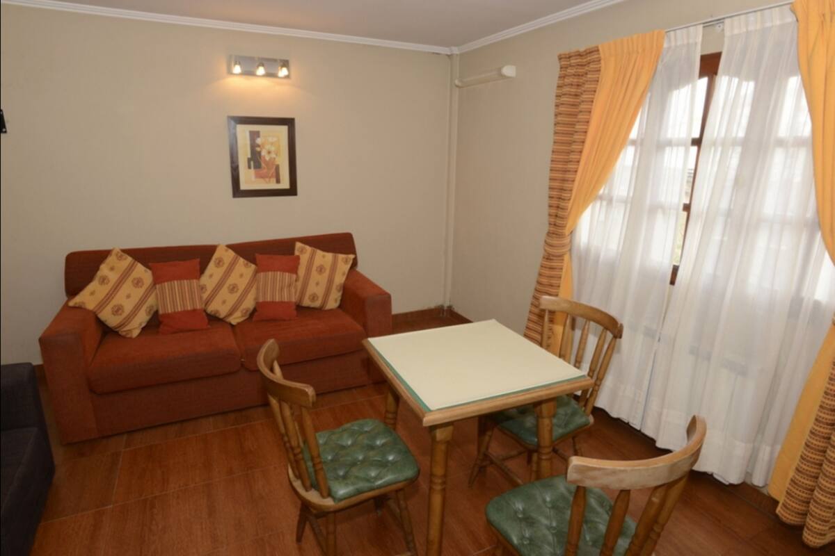 Ein Wohnzimmer mit einer Couch, zwei Sesseln, einem kleinen Tisch und einem Fenster mit Vorhängen.
