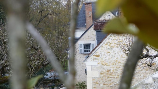 Un edificio de piedra con una chimenea, un balcón pequeño y mesas al aire libre.