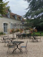 Une cour avec des sièges en plein air, une pergola ornée de fleurs et un bâtiment doté d’un toit en tuiles.