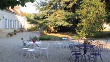 An outdoor seating area with tables and chairs, surrounded by gravel and plants, with a building in the background.