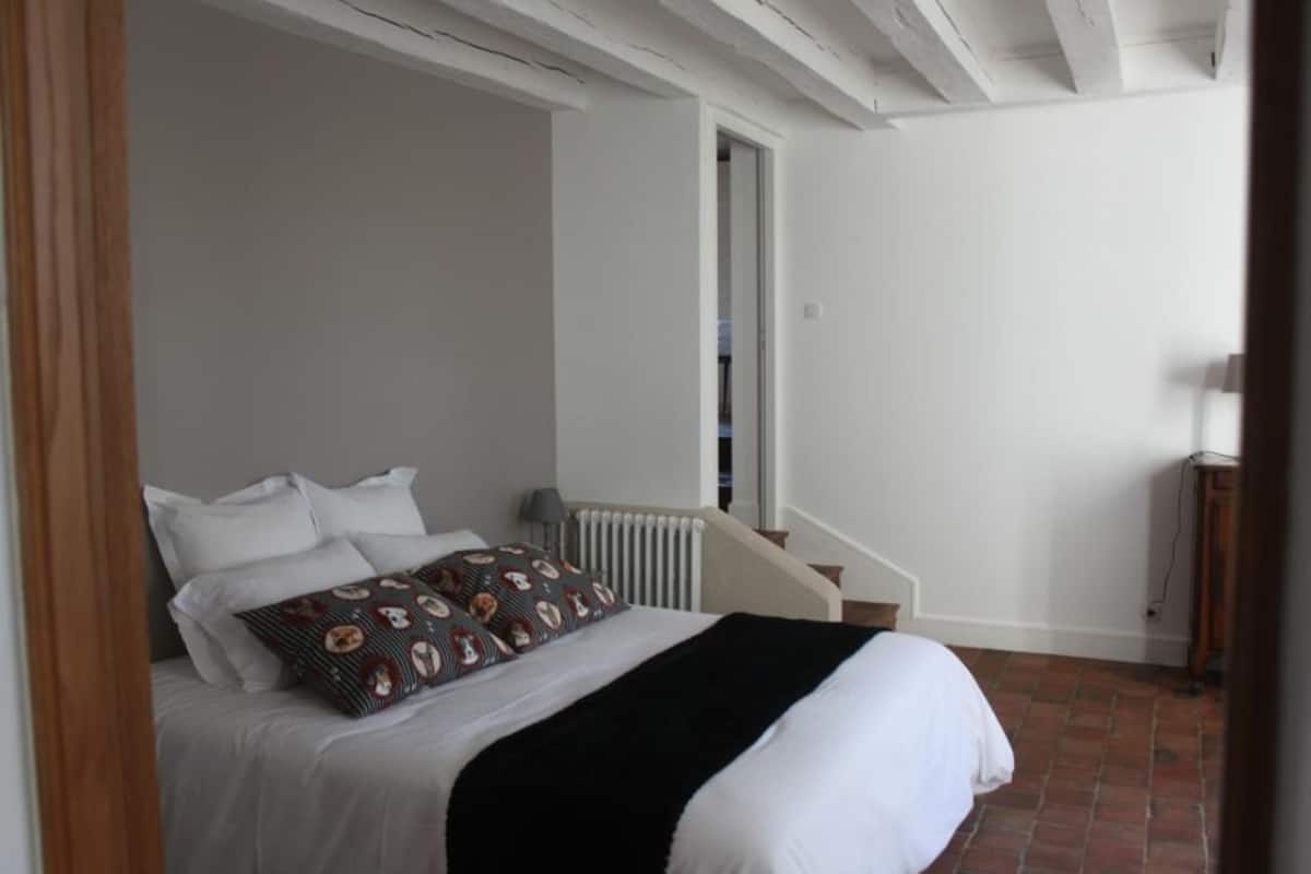 Ein Schlafzimmer mit Bett, weißen Wänden, einer Heizung und einer Treppe.