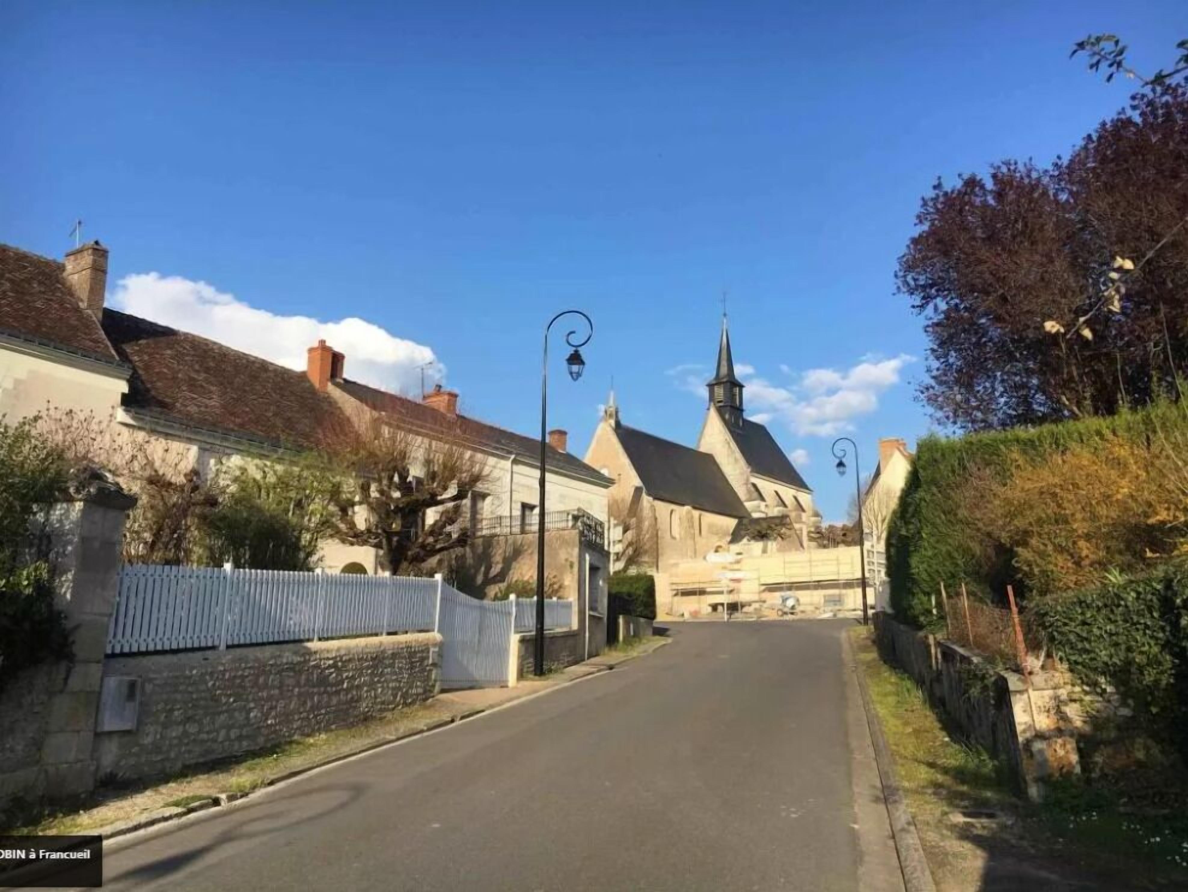 A narrow street with traditional buildings, a church, and a white fence.