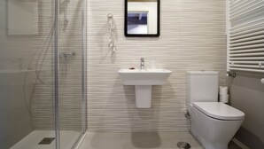 A modern bathroom with a glass shower enclosure, a white sink, and a toilet. - Pensión Domus Gallery (Arzua)