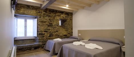 A bedroom with two beds, a stone wall, wooden beams, a window, and a TV.