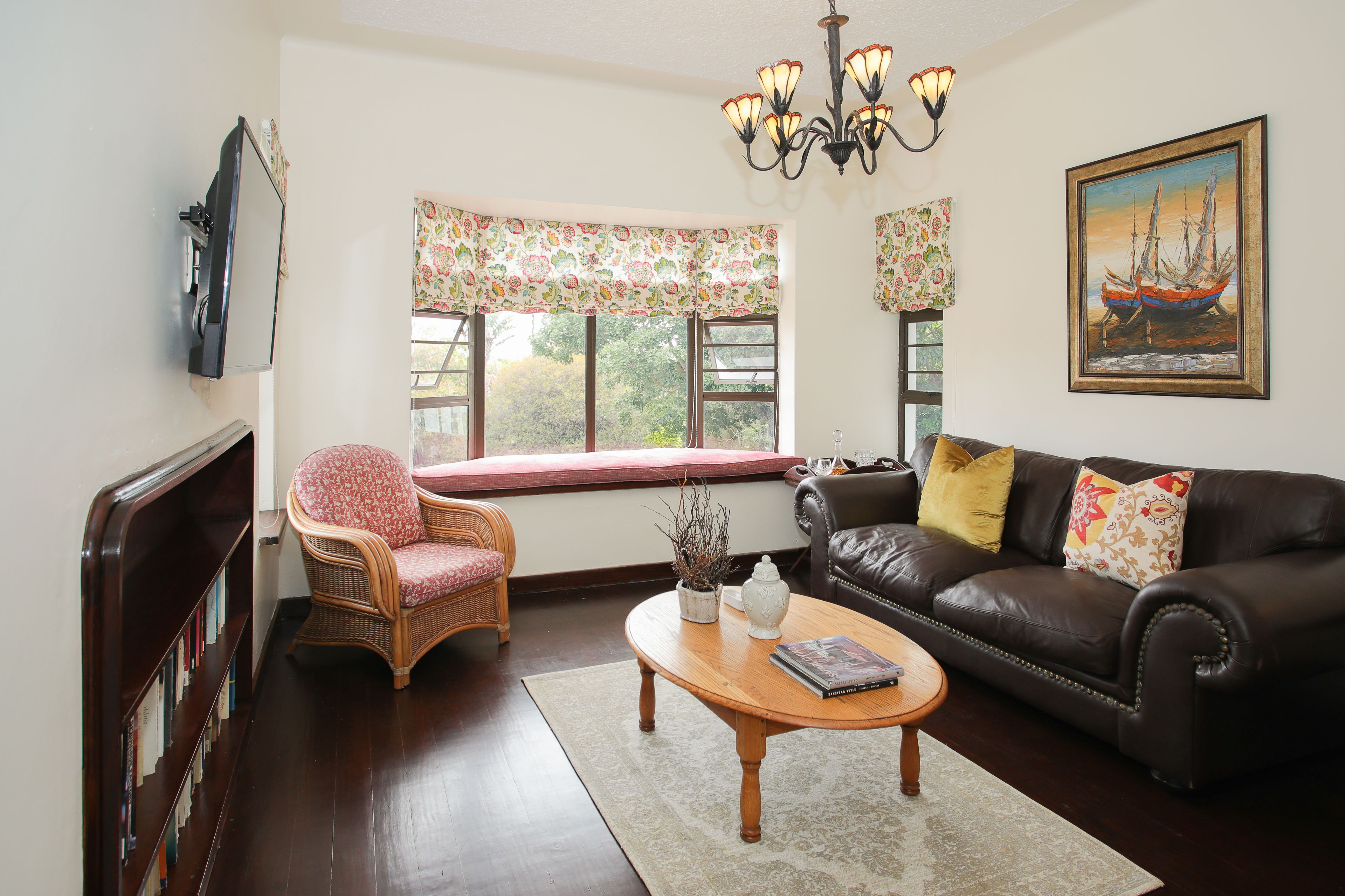 A living room with a brown leather sofa, a wicker chair, a wooden coffee table, and a bookshelf.