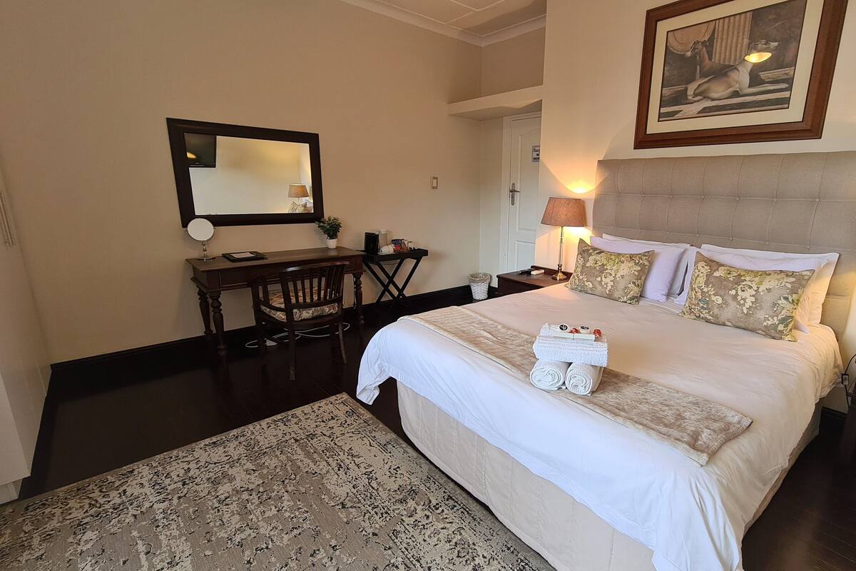A hotel room with a large bed, a desk, a chair, a mirror, and two bedside lamps.