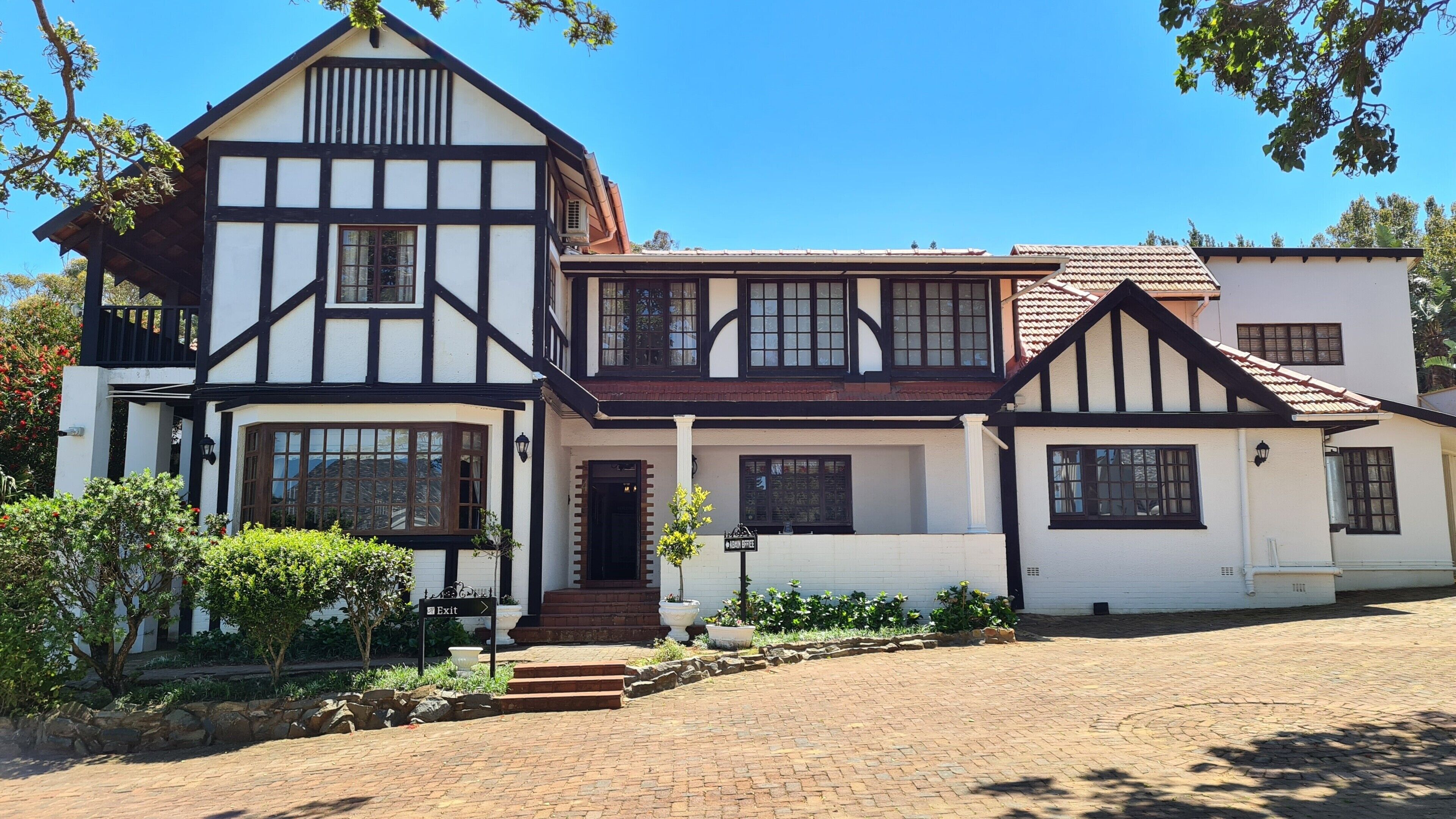 A traditional Tudor-style building with a symmetrical facade, multiple windows, and a central entrance with steps leading up to it.
