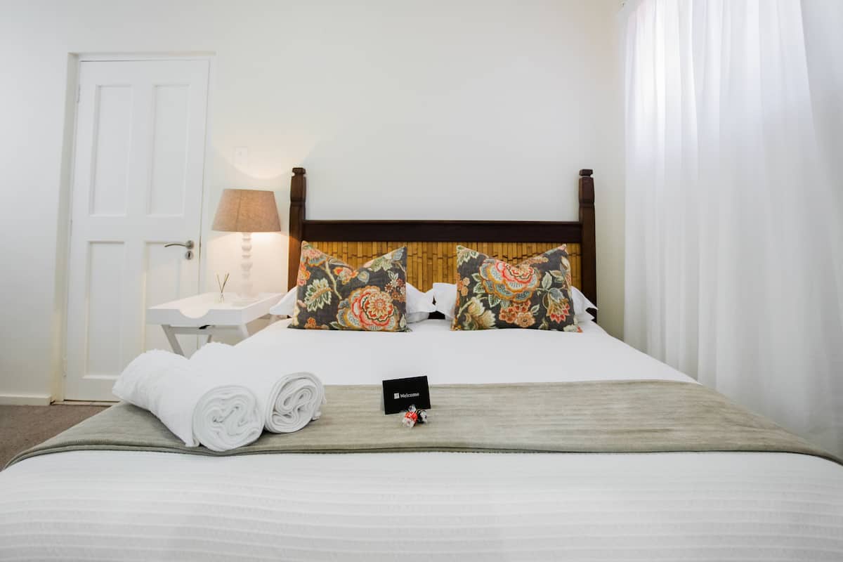 A neatly made bed with floral pillows, a rolled white towel, and a welcome card on a bedspread.