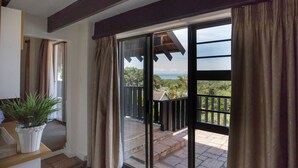 Een kamer met een schuifglazen deur die uitkomt op een balkon met uitzicht op groen en de zee.