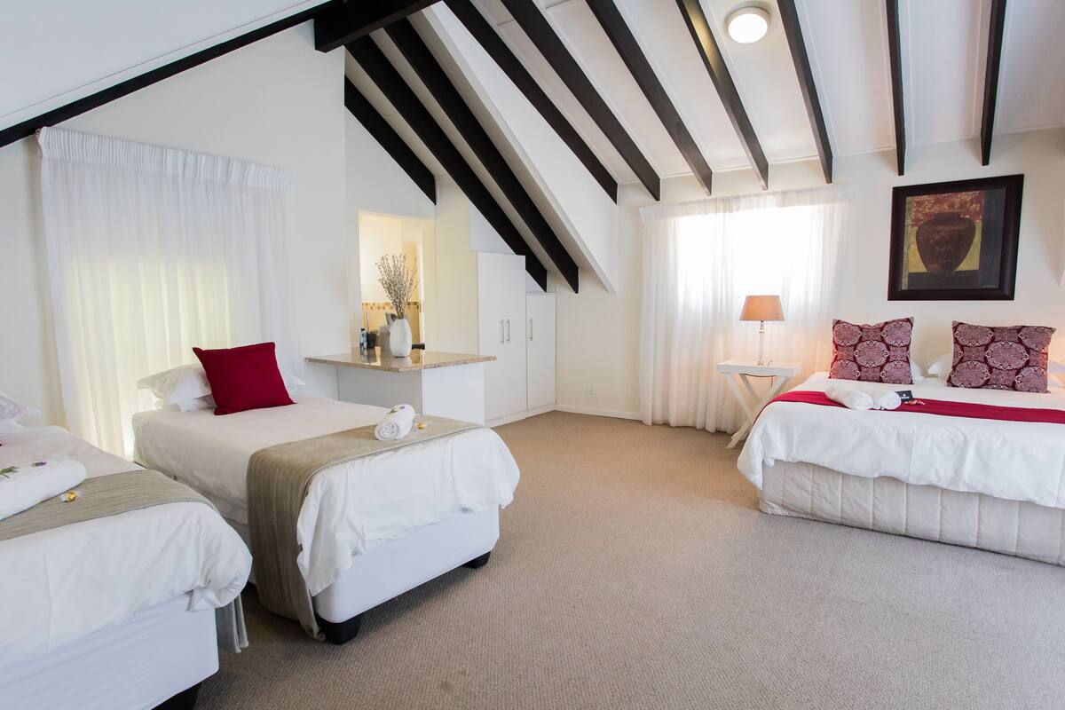 A hotel room with two beds, a small table, a lamp, and a painting on the wall.