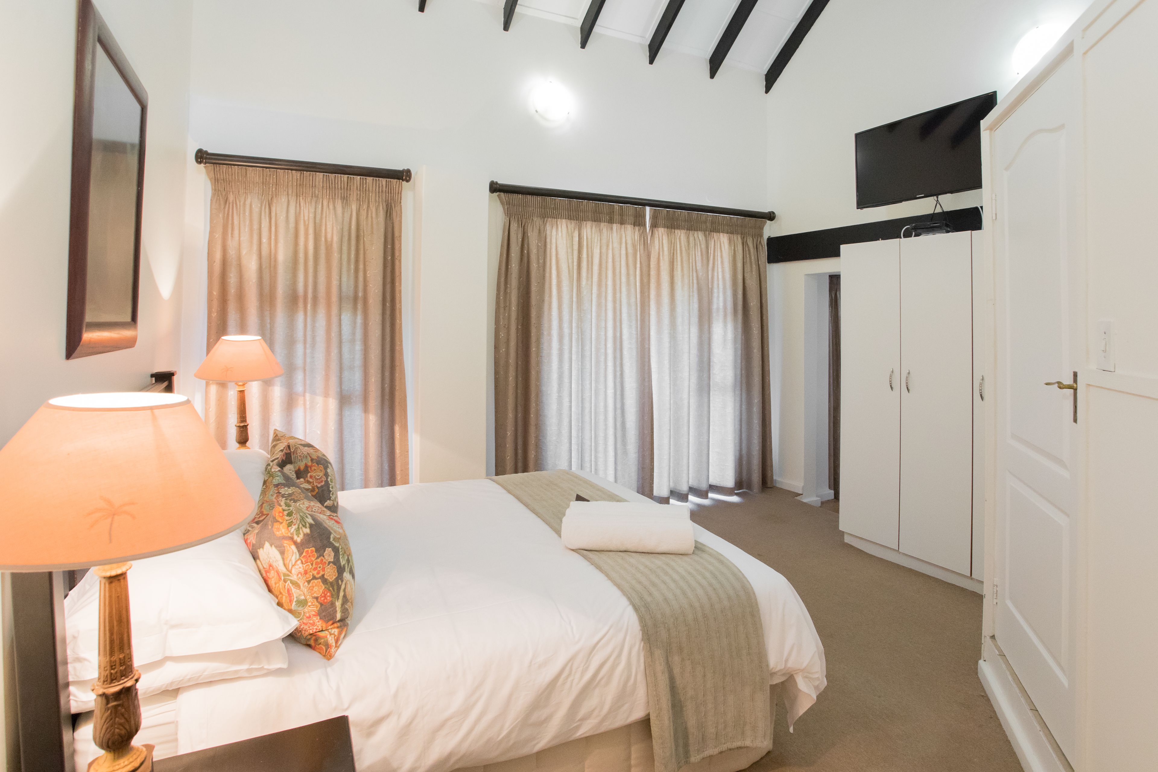 A bedroom with a bed, a lamp, curtains, a TV, and a wardrobe.