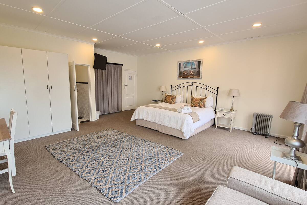 A hotel room with a bed, bedside tables, a desk, a chair, and a wardrobe.