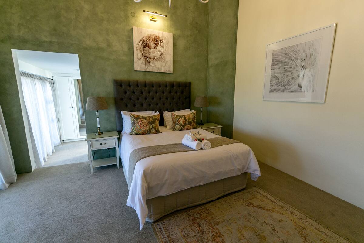 A bedroom with a large bed, two bedside tables, a headboard, and artwork on the walls.