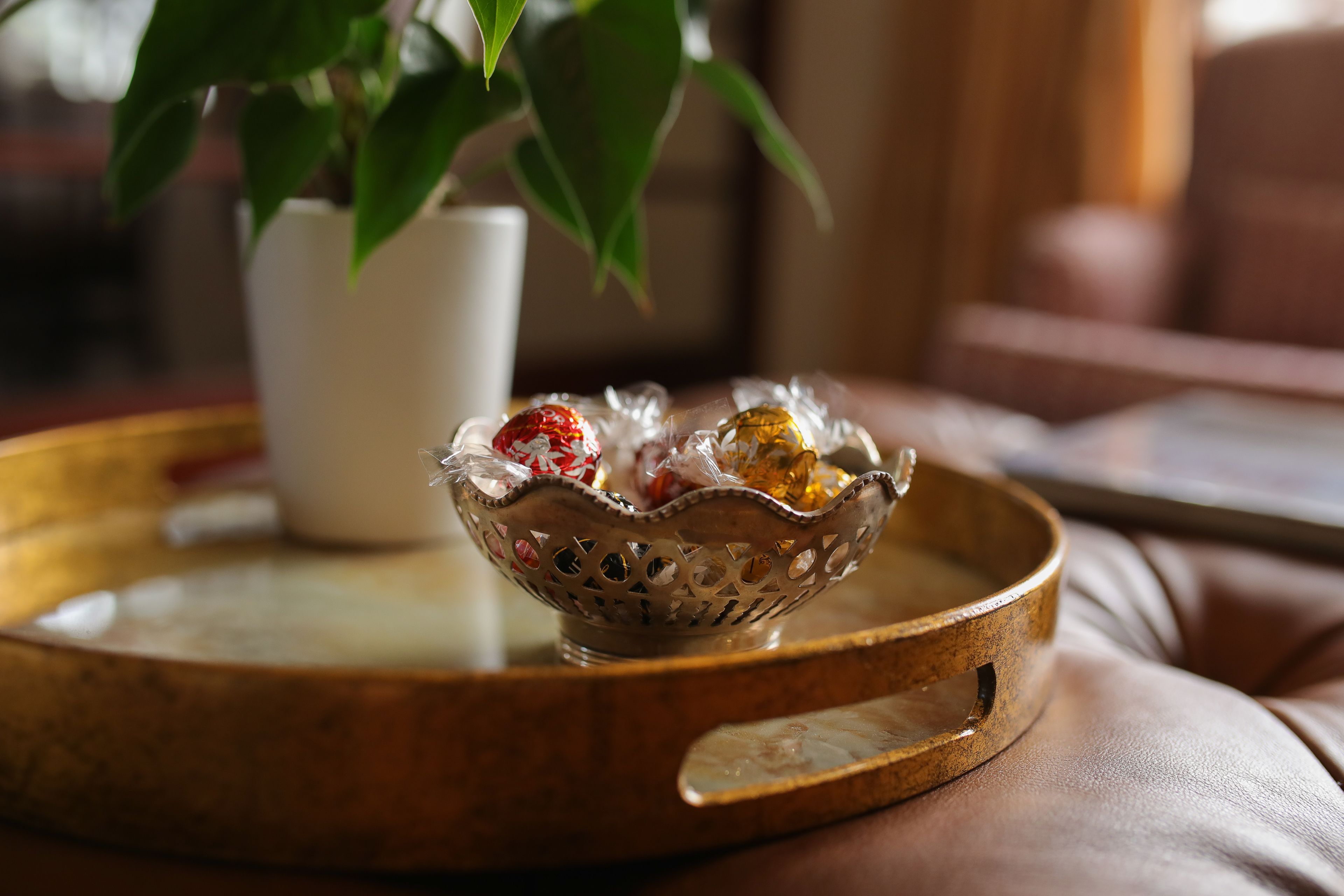 A tray with a decorative bowl containing chocolates, a white cup, and a potted plant.