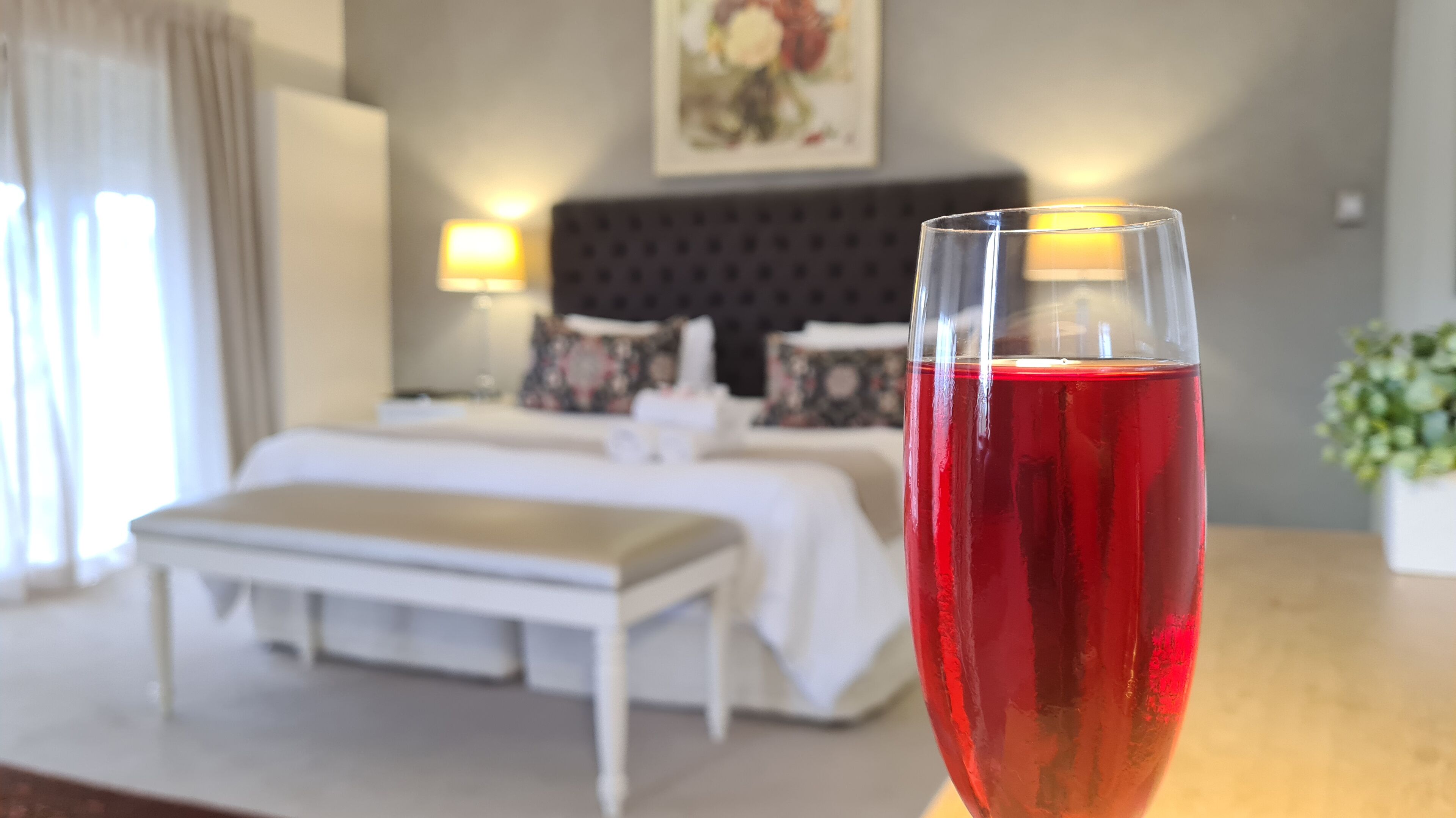 Hotelkamer met een bed, bedlampen, een nachtkastje met een glas rode drank en een schilderij aan de muur.