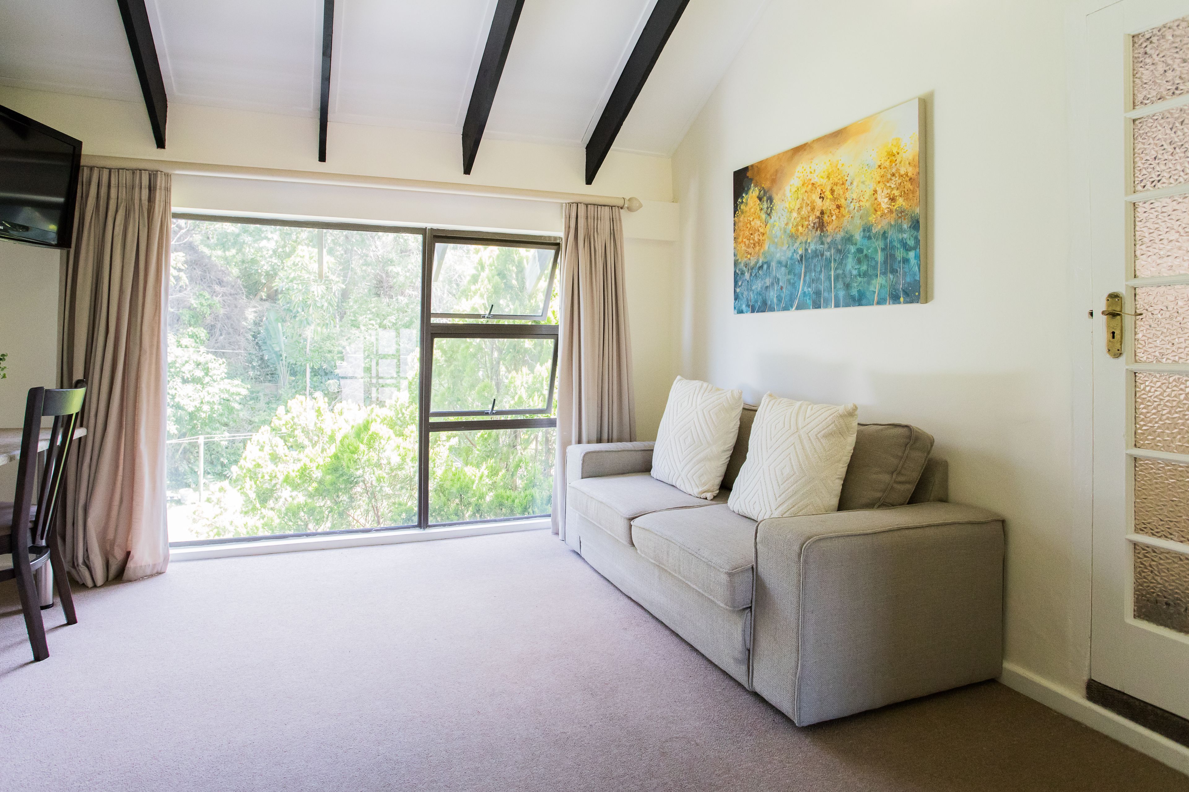 A living room with a large window, a sofa, and a painting on the wall.