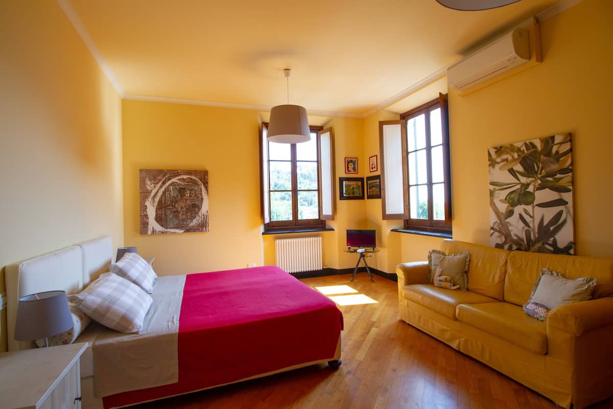 Quarto com uma cama, um sofá amarelo, uma mesinha e um radiador.