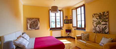 A room with a bed, a yellow sofa, a small table, and a radiator.