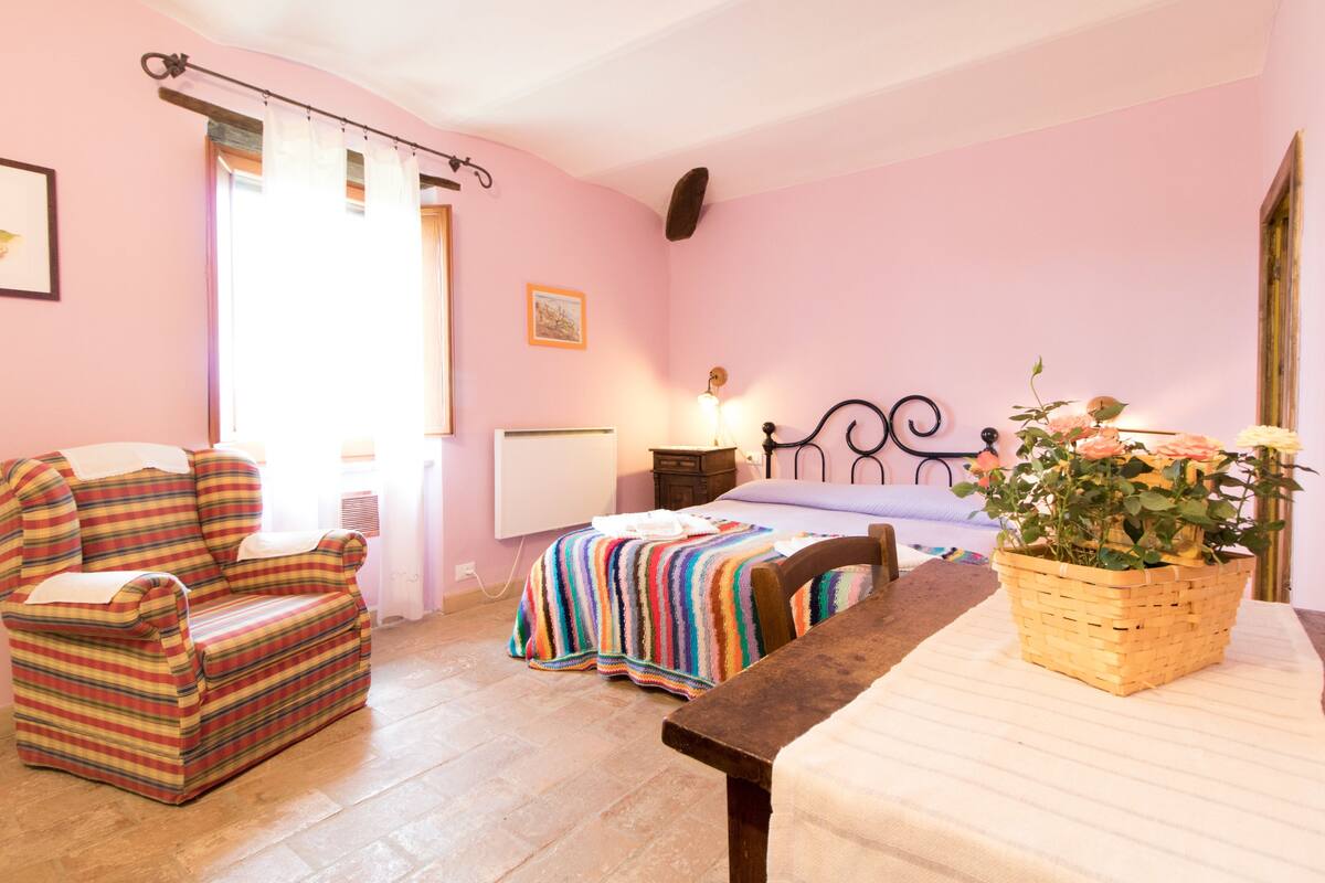 Een gezellige slaapkamer met een bed, een stoel, een tafel en een raam met gordijnen.