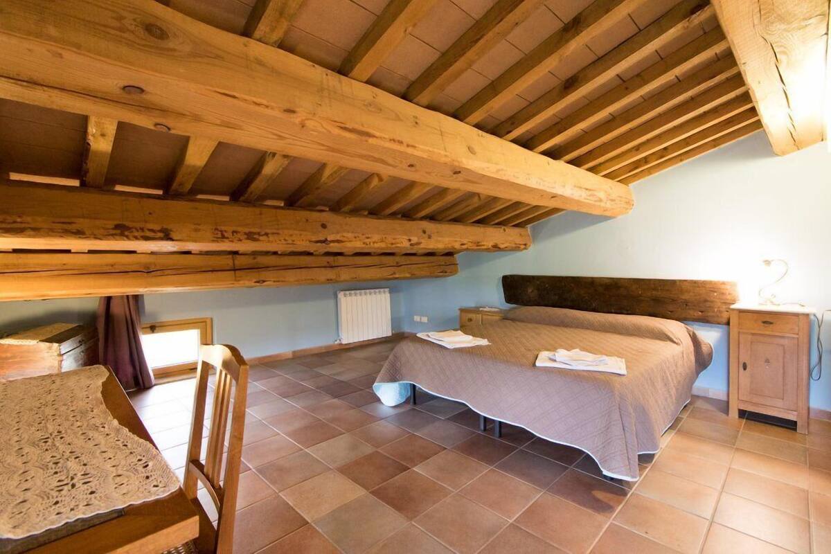 Een slaapkamer met een houten plafond, een bed, een nachtkastje en een stoel.