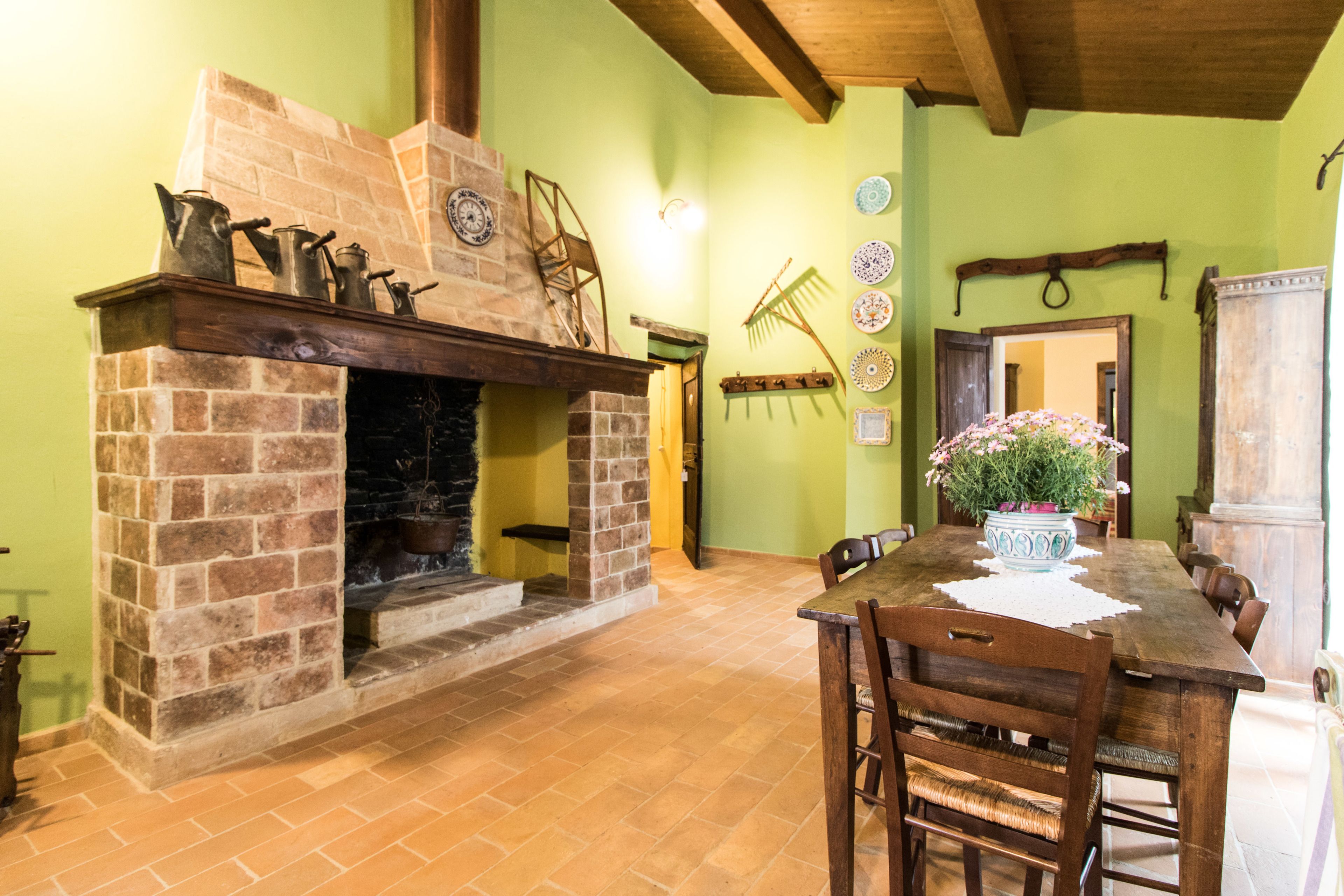 A dining area with a brick fireplace, wooden ceiling beams, and a table with chairs.
