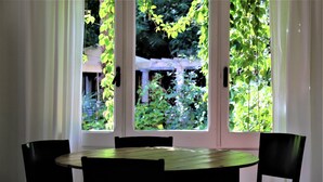 A dining area with a round table and four chairs, a window with greenery outside, and a white curtain. - Hostal Montsoliu (Arbucies)